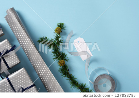 Gift wrapping materials. Rolls of wrapping paper, ribbon, ready-wrapped gifts, spruce branches. Blue background, space for your text. Preparing for the holidays 127858783