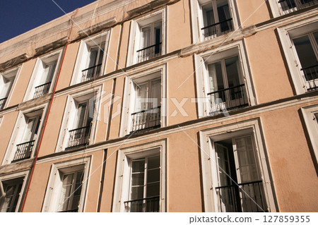 Facade of an apartment block building in old Spanish town. Yellow beige house wall with many windows, balconies with wooden shutters bottom view. 127859355