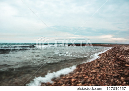 Sandy sea, ocean coast with waves crashing on a sandy shore on a summer day. Vertical natural seaside background. Marine theme. Wavy windy weather. 127859367