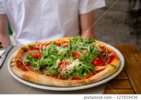 Fresh Italian pizza with arugula, cherry tomatoes, prosciutto and parmesan served at outdoor cafe 127859436
