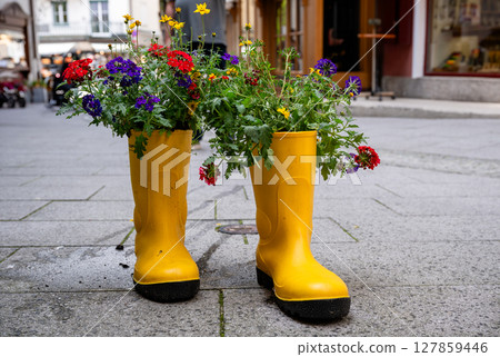 Bright yellow rubber boots repurposed as flower planters on a city street 127859446