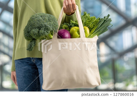 Woman Holding Reusable Grocery Bag with Fresh Organic Vegetables in Modern Urban Setting Woman Holding Reusable Grocery Bag with Fresh Organic Vegetables in Modern Urban Setting 127860016
