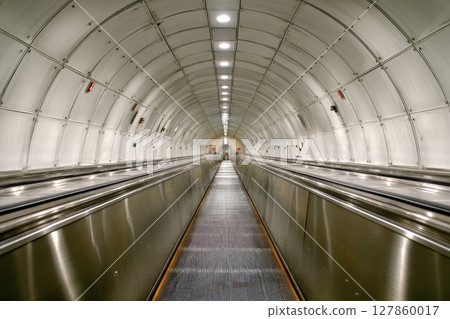 A long, narrow, silver and gray tunnel with a silver escalator A long, narrow, silver and gray tunnel with a silver escalator 127860017