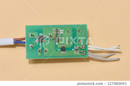 Green electronic board with components and some wires placed on beige background. 127860041
