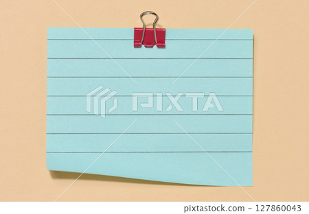 Blue sticky note secured with a red paper clip, centered on a beige background. 127860043