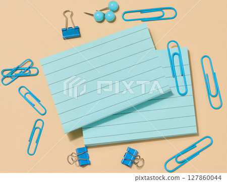 Several stacks of light blue sticky notes and many blue paper clips of various shapes, arranged on a beige background. Several stacks of light blue sticky notes and many blue paper clips of various shapes, arranged on a beige background. 127860044