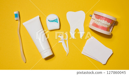 Toothbrush, white tube of toothpaste, dental floss in a case, white tooth cut out of paper, model of dentures on a bright yellow background. 127860045
