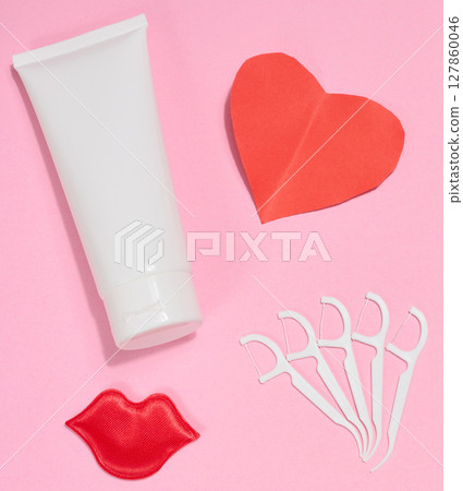 White tube of toothpaste, red paper heart, red decorative lips and plastic dental floss holders placed on pink background. White tube of toothpaste, red paper heart, red decorative lips and plastic dental floss holders placed on pink background. 127860046