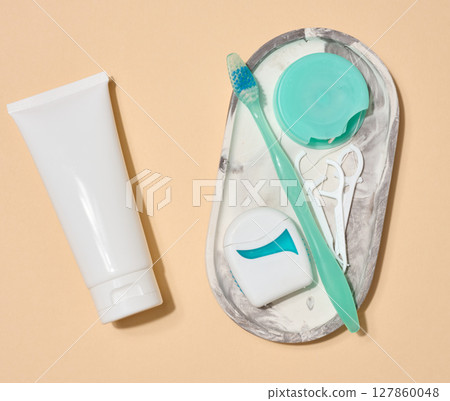 Set of oral hygiene items, tube of toothpaste, toothbrush, dental floss placed on small oval tray, on beige background. Top view Set of oral hygiene items, tube of toothpaste, toothbrush, dental floss placed on small oval tray, on beige background. Top view 127860048