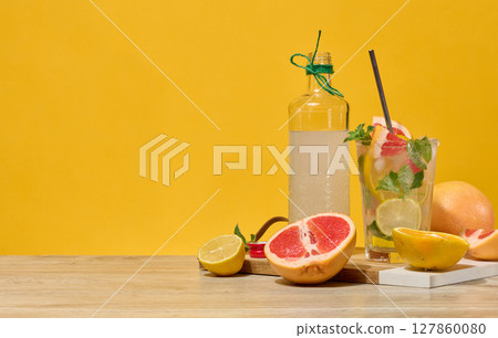 Fresh citrus drink with lemon, grapefruit, and mint in a glass with ice cubes and a straw. Surrounded by fresh citrus fruits and a bottle of homemade lemonade. Fresh citrus drink with lemon, grapefruit, and mint in a glass with ice cubes and a straw. Surrounded by fresh citrus fruits and a bottle of homemade lemonade. 127860080