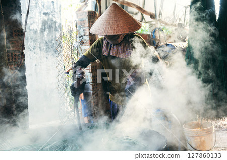 Vietnamese female worker in straw hat works in a reed dyeing workshop at wicker mat factory in Vietnam Vietnamese female worker in straw hat works in a reed dyeing workshop at wicker mat factory in Vietnam 127860133