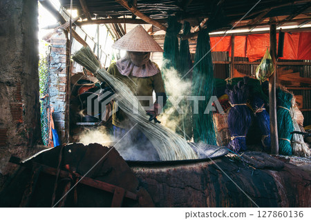 Vietnamese woman in straw hat dyes reeds at a woven sleeping factory in Vietnam Vietnamese woman in straw hat dyes reeds at a woven sleeping factory in Vietnam 127860136