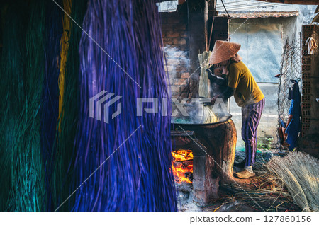 Vietnamese woman in a traditional straw hat works in reed dyeing workshop for production of woven mats in Vietnam 127860156