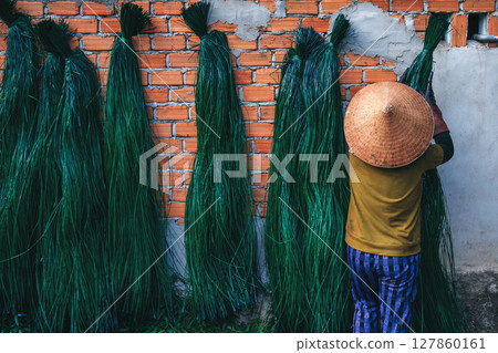 Vietnamese woman in traditional straw hat dries dyed reeds at a woven mat factory in village in Vietnam 127860161
