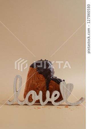 LOVE word wooden decoration Delicious fresh croissant topped with Dark chocolate flavor Ganache. Creation unique heart shape bakery. Puff pastry holiday love gift present idea Valentine's day 127860580