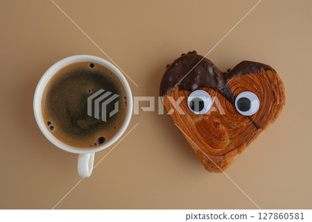Flat lay Latte cappuccino coffee drink creative idea with personalized funny eyes on Delicious fresh croissant topped with Dark chocolate flavor Ganache. Creation unique heart shape bakery. Puff 127860581