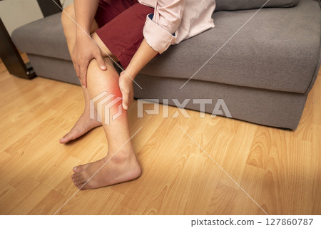 Man sitting on the couch and suffering from leg pain at home. Healthcare concept Man sitting on the couch and suffering from leg pain at home. Healthcare concept 127860787