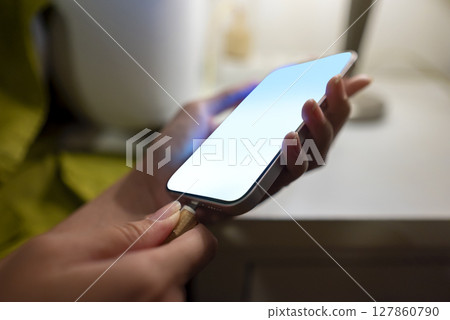 Woman lying down on a bed and charging her cellphone at night before sleep at home 127860790
