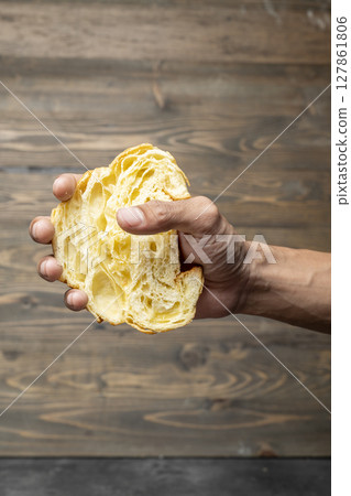 Closeup view human hand holding a slice of a freshly baked croissant with a wooden background Closeup view human hand holding a slice of a freshly baked croissant with a wooden background 127861806