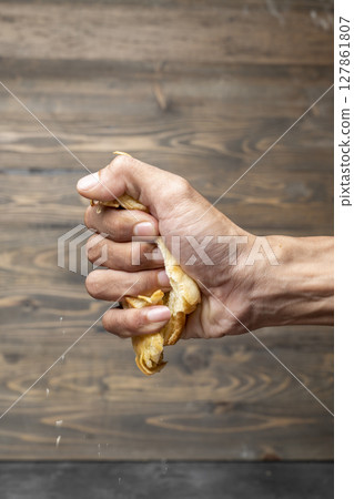 Closeup view human hand breaking a slice of a freshly baked croissant with a wooden background Closeup view human hand breaking a slice of a freshly baked croissant with a wooden background 127861807