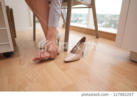 Businesswoman sitting and feels an ache because of wearing high heels for too long in a hybrid workplace. Business concept. Remote working from home Businesswoman sitting and feels an ache because of wearing high heels for too long in a hybrid workplace. Business concept. Remote working from home 127862267
