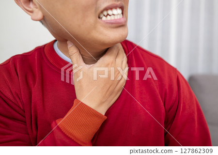 Indonesian southeast asian man sitting on the couch at home and coughing. Suffers from an attack of asthma or allergies. Healthcare concept Indonesian southeast asian man sitting on the couch at home and coughing. Suffers from an attack of asthma or allergies. Healthcare concept 127862309
