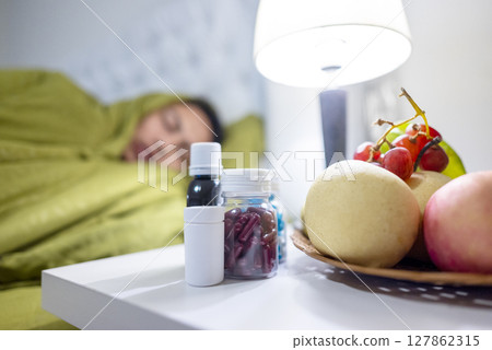 Indonesian southeast asian man in a blanket sleeping on the bed at home. Suffer from fever, flu, and cold. Medicine and fruit on the bedside. Healthcare and medical concept 127862315