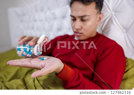Indonesian southeast asian man sitting on the bed at home gets medicine for coughing. Suffer from fever, flu, and cold. Healthcare and medical concept 127862316