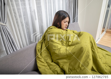 Indonesian southeast asian woman in a blanket sitting on the couch at home and coughing. Suffer from fever, flu, and cold. Healthcare concept Indonesian southeast asian woman in a blanket sitting on the couch at home and coughing. Suffer from fever, flu, and cold. Healthcare concept 127862785