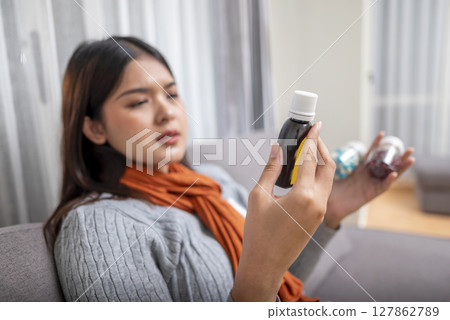 Indonesian southeast asian woman in a scarf sitting on the couch at home gets medicine for coughing. Suffer from fever, flu, and cold. Healthcare and medical concept 127862789