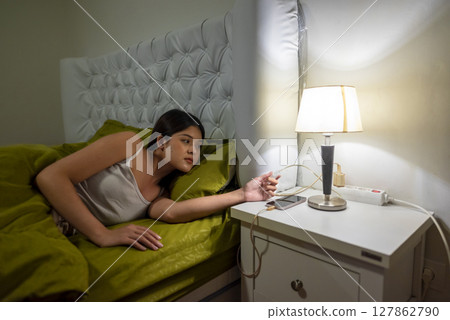 Indonesian southeast asian woman hand pushes the button on the white switch to turn off the lamp standing on the bedside table. Self-care and wellness routines concept Indonesian southeast asian woman hand pushes the button on the white switch to turn off the lamp standing on the bedside table. Self-care and wellness routines concept 127862790