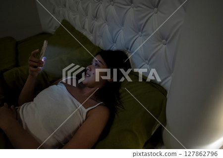 Indonesian southeast asian woman lying down on a bed and using a cellphone at night before sleep at home Indonesian southeast asian woman lying down on a bed and using a cellphone at night before sleep at home 127862796
