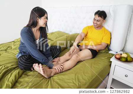 Indonesian southeast asian woman massages her husband feet in the bedroom. Self-care and wellness routines concept Indonesian southeast asian woman massages her husband feet in the bedroom. Self-care and wellness routines concept 127862982