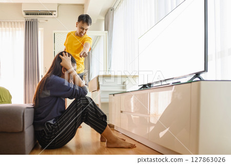 Indonesian southeast asian couple arguing at home in front of television with anger and depression. Mental health and mindfulness concept. Empty television screen for mockup, template, or copy space Indonesian southeast asian couple arguing at home in front of television with anger and depression. Mental health and mindfulness concept. Empty television screen for mockup, template, or copy space 127863026