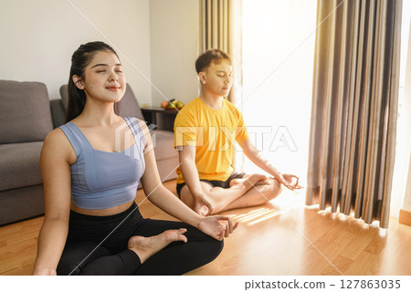 Indonesian southeast asian couple meditating in the lotus position on yoga at home for a healthy lifestyle and body care. Meditation and yoga practices concept 127863035