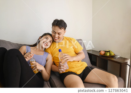 Indonesian southeast asian couple drinking water after finishing a home body workout exercise session for a fit physique and a healthy sport lifestyle at home. Fitness and active lifestyles concept Indonesian southeast asian couple drinking water after finishing a home body workout exercise session for a fit physique and a healthy sport lifestyle at home. Fitness and active lifestyles concept 127863041