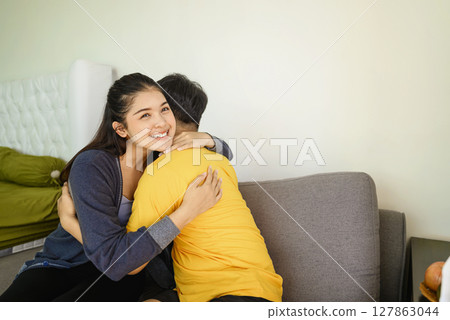 Indonesian southeast asian affectionate couple embracing while sitting on the couch at home Indonesian southeast asian affectionate couple embracing while sitting on the couch at home 127863044