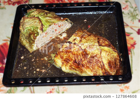 meatloaf in Savoy cabbage leaves, oven-baked in baking tray full of its own juice. piece is cut out of the middle, texture of a dense cooked minced meat with vegetables is visible on the cut 127864608