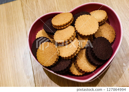 close up of chocolate and butter cream biscuits cookies on a pink heart plate with copy space 127864994