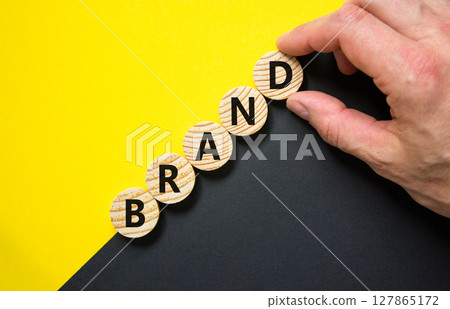 Brand symbol. Concept word Brand on beautiful wooden circles. Beautiful yellow and black background. Businessman hand. Business brand concept. Copy space. 127865172