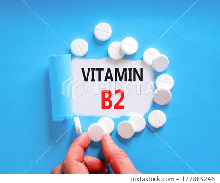 Vitamin B2 riboflavin symbol. Concept words Vitamin B2 on beautiful white paper. White pills tablets. Doctor's hand. Beautiful blue background. Medical healthy lifestyle Vitamin B2 riboflavin concept. 127865246