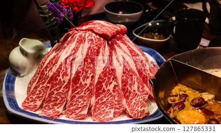 close up of slices of raw uncooked marbled beef in a hill for hot pot. The spicy hot pot on the side close up of slices of raw uncooked marbled beef in a hill for hot pot. The spicy hot pot on the side 127865331