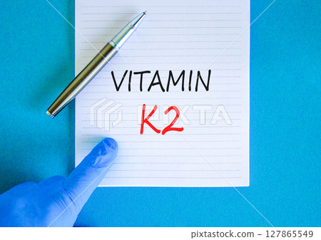 Vitamin K2 phylloquinone symbol. Concept words Vitamin K2 on beautiful note. Doctor's hand in blue medical glove. Beautiful blue background. Medical healthy lifestyle Vitamin K2 phylloquinone concept. 127865549