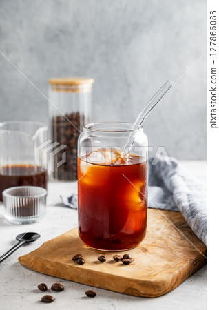 Cold brew coffee in a glass with ice on a wooden board on a light background with coffee beans 127866083
