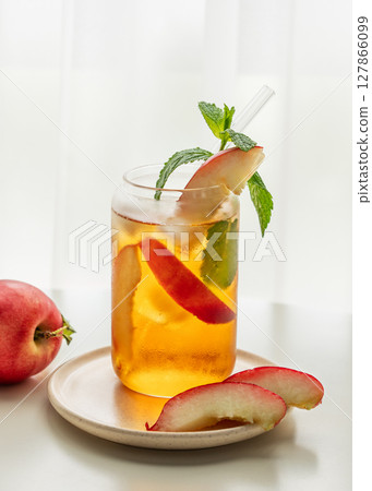 Ice tea with peach, mint in a glass on a white table near window with fresh fruits and sunlight. 127866099