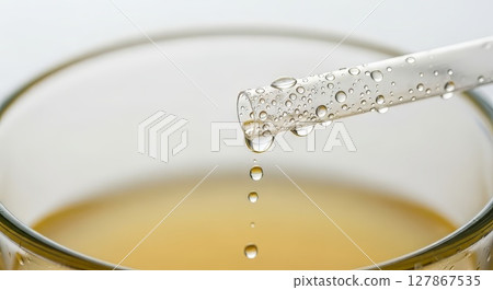 Macro Water Droplets Dripping from Condensation Covered Glass Pipette into Yellow Liquid 127867535