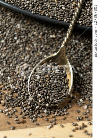 Chia seeds in a spoon on a wooden background, close-up. 127867803