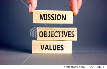 Mission objectives values symbol. Concept words Mission Objectives Values on beautiful blocks. Beautiful grey background. Businessman hand. Business mission objectives values concept. Copy space. 127868611