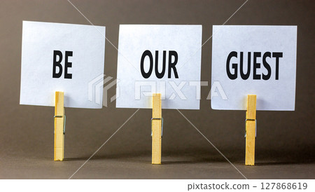 Be our guest symbol. Concept words Be our guest on beautiful white paper on wooden clothespin. Beautiful grey background. Business and be our guest concept. Copy space. 127868619