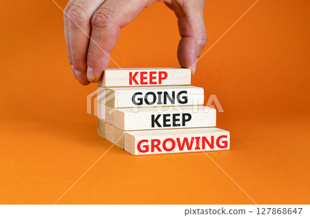 Keep going and growing symbol. Concept words phrase Keep going keep growing on beautiful wooden blocks. Beautiful orange background. Businessman's hand. Business Keep going growing concept. Copy space 127868647
